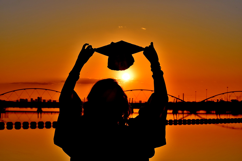 Girl holding a graduation cap with a sunset in the background
