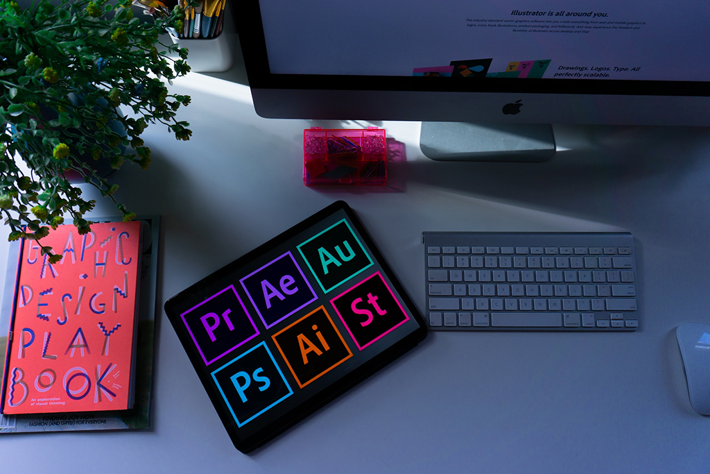 A computer screen partially shown with adobe apps logos being shown on a rectangle on a desk